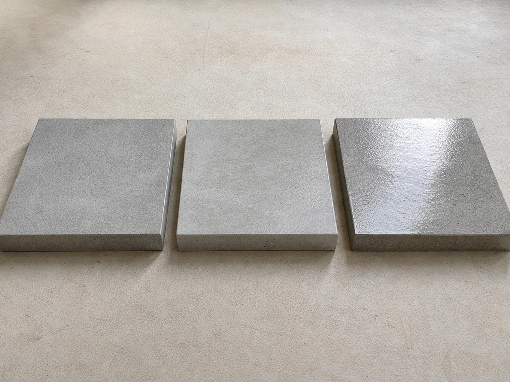 Three concrete sealer test panels showing matte, satin, and gloss finishes with different reflectivity.